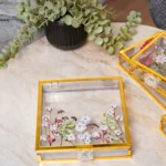 Clear acrylic memory boxes with pressed flower designs and gold frames.