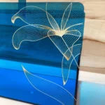 Close-up of golden floral print on blue acrylic surface.
