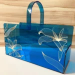 Side view of long blue acrylic printed basket with handles.