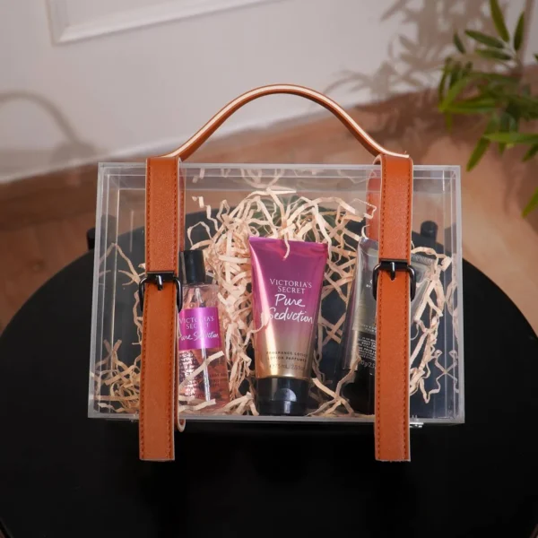 Clear acrylic suitcase box with tan leather straps placed on a black table.