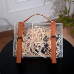 Front view of transparent box with stitched leather strap accents.