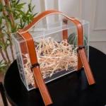Top angle of acrylic suitcase gift box with shredded filler inside.
