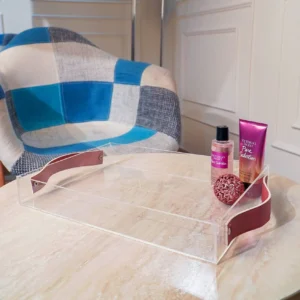 Clear acrylic serving tray with maroon leather side grips placed on marble table with toiletries.
