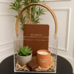 Transparent acrylic gift box with mustard leather handle on black table with decor inside.