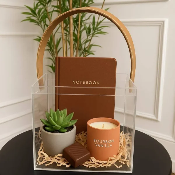 Transparent acrylic gift box with mustard leather handle on black table with decor inside.