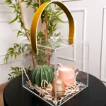 Side angle of clear cube gift box showcasing mustard leather handle and contents.